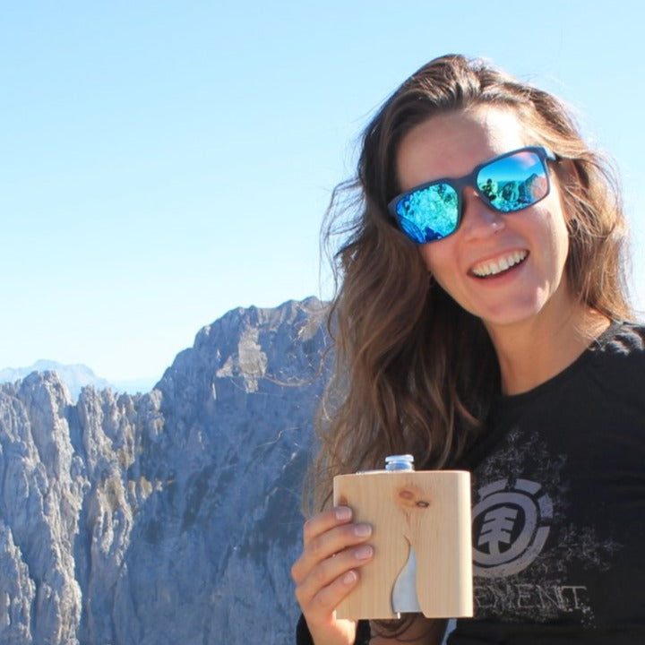 Wandererin steht auf dem Gipfel und hat einen Holzflachmann in der Hand