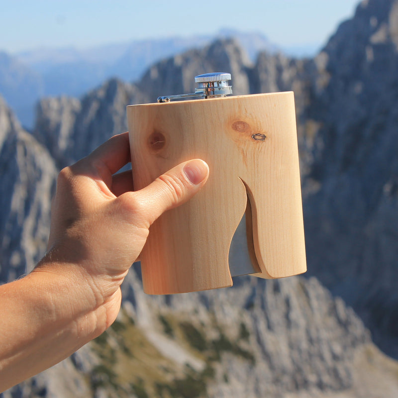 der Flachmann wird von einer Hand gehalten im Hintergrund sieht man herrliches Bergpanorama